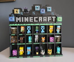 20260425_102231 Czarna półka na figurki w stylu Minecraft z kolorowymi postaciami i zielonymi wymiennymi napisami na biurku